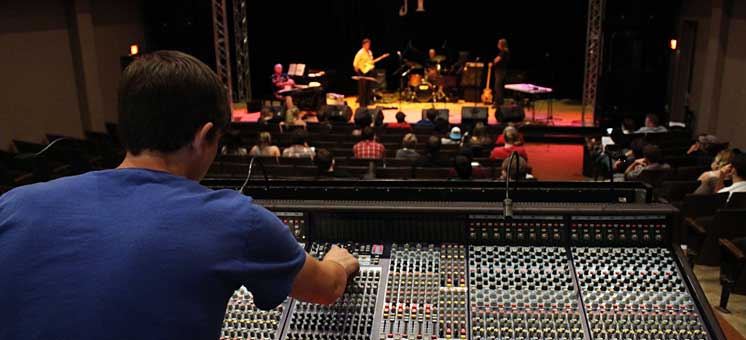 Photo of Front of House Mixing Engineer  at soundboard front of house with view of stage